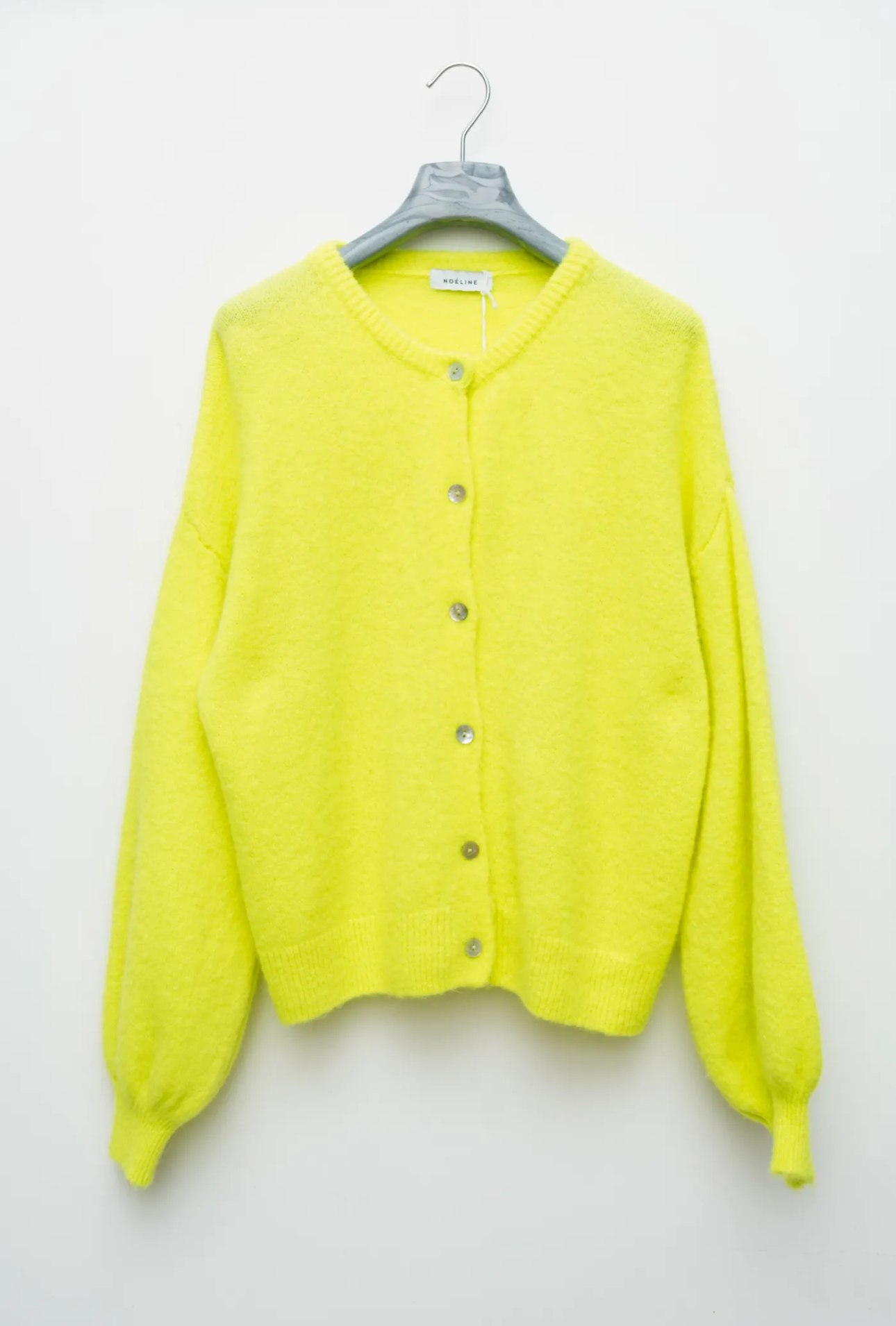 A neon yellow cardigan sweater hanging on a gray hanger against a plain white wall, featuring a round neckline, front button closure, and balloon sleeves.