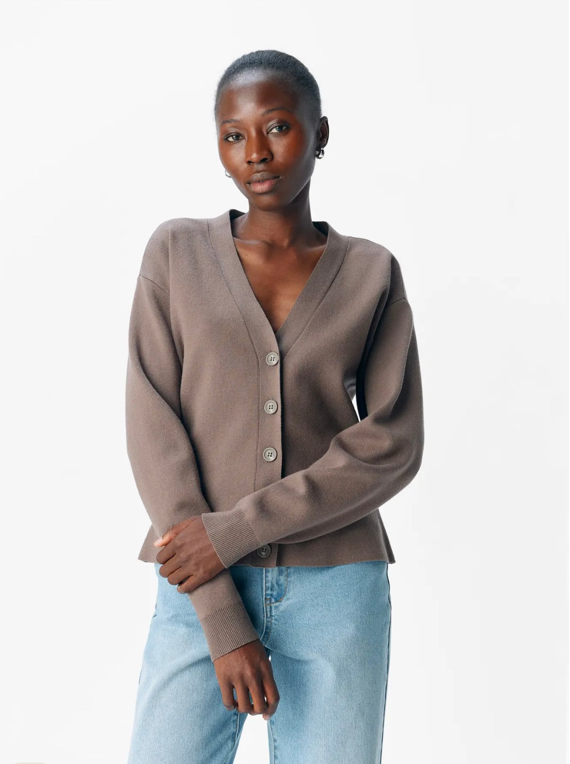 Woman wearing a brown cardigan and light blue jeans on a white background