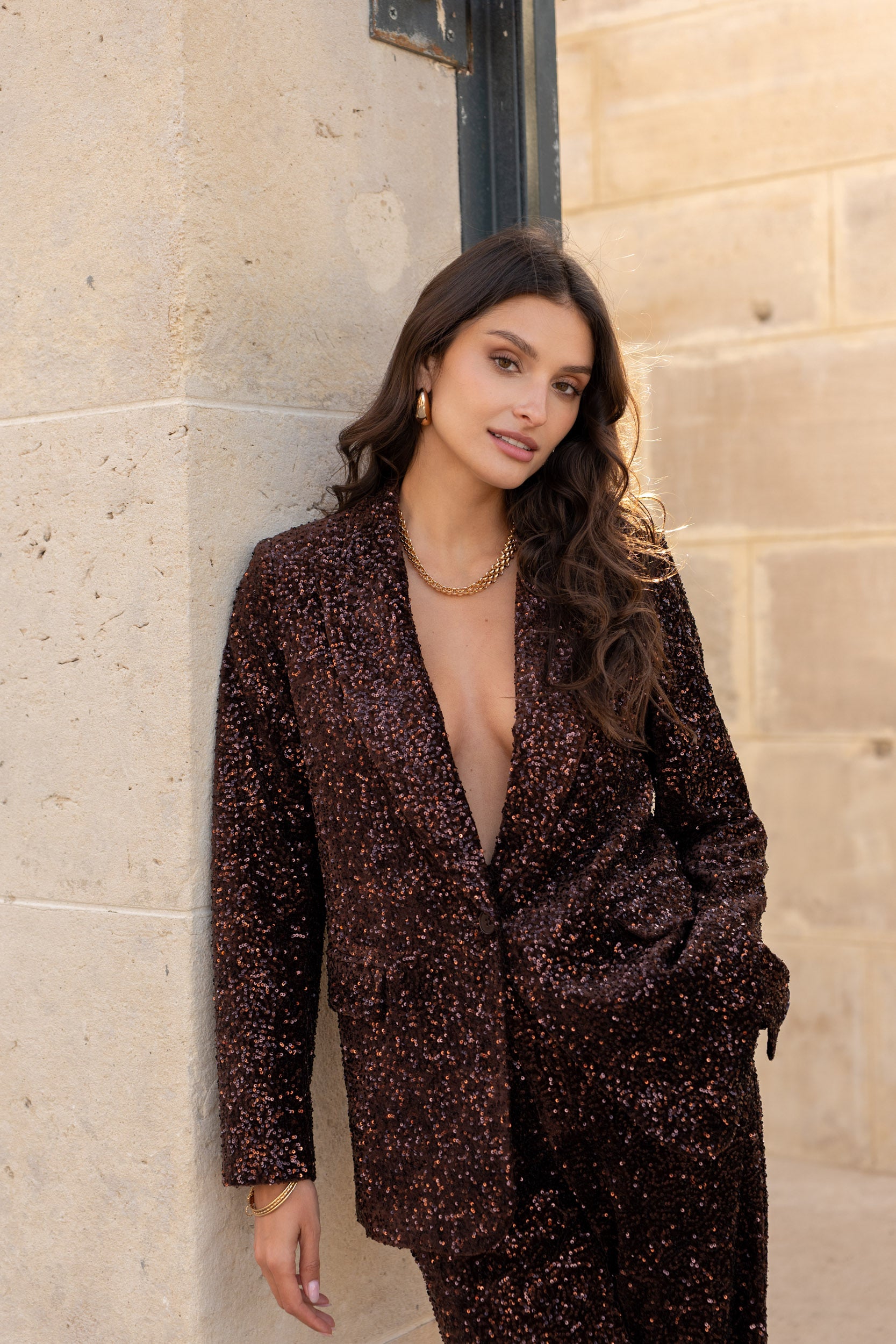 Woman wearing a dark brown patterned outfit against a stone wall.