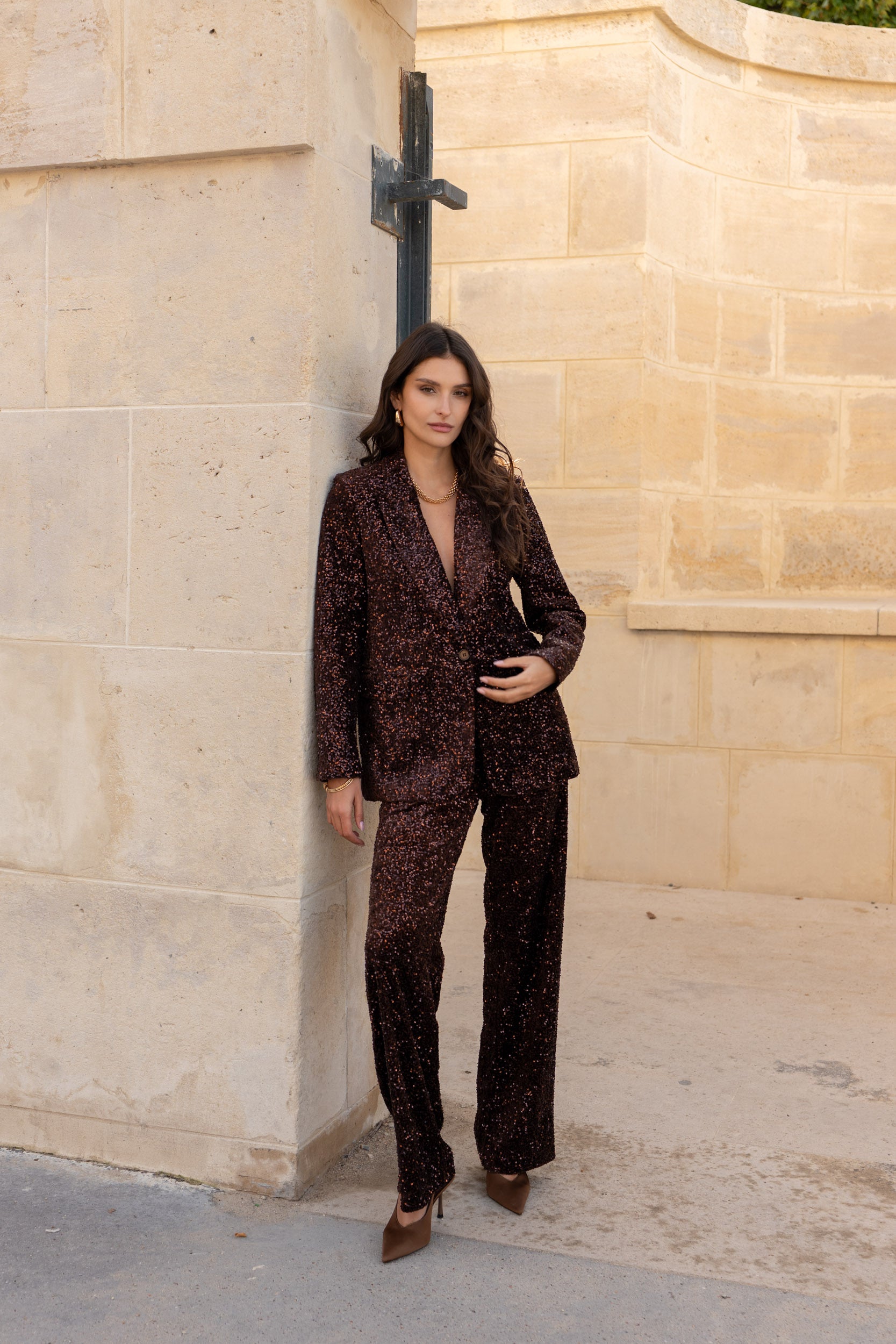 Woman in a patterned suit standing against a beige stone wall.