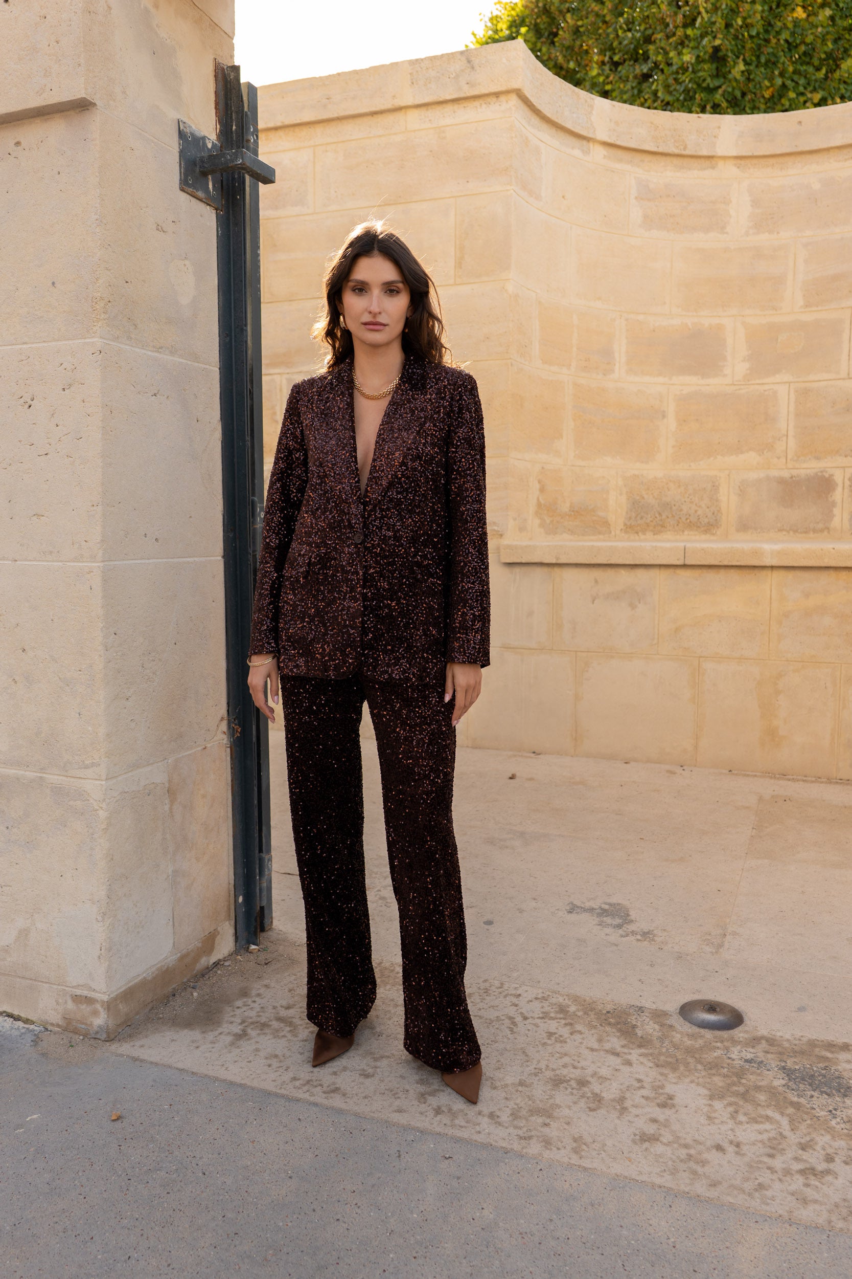 Woman in a patterned suit standing against a beige wall.