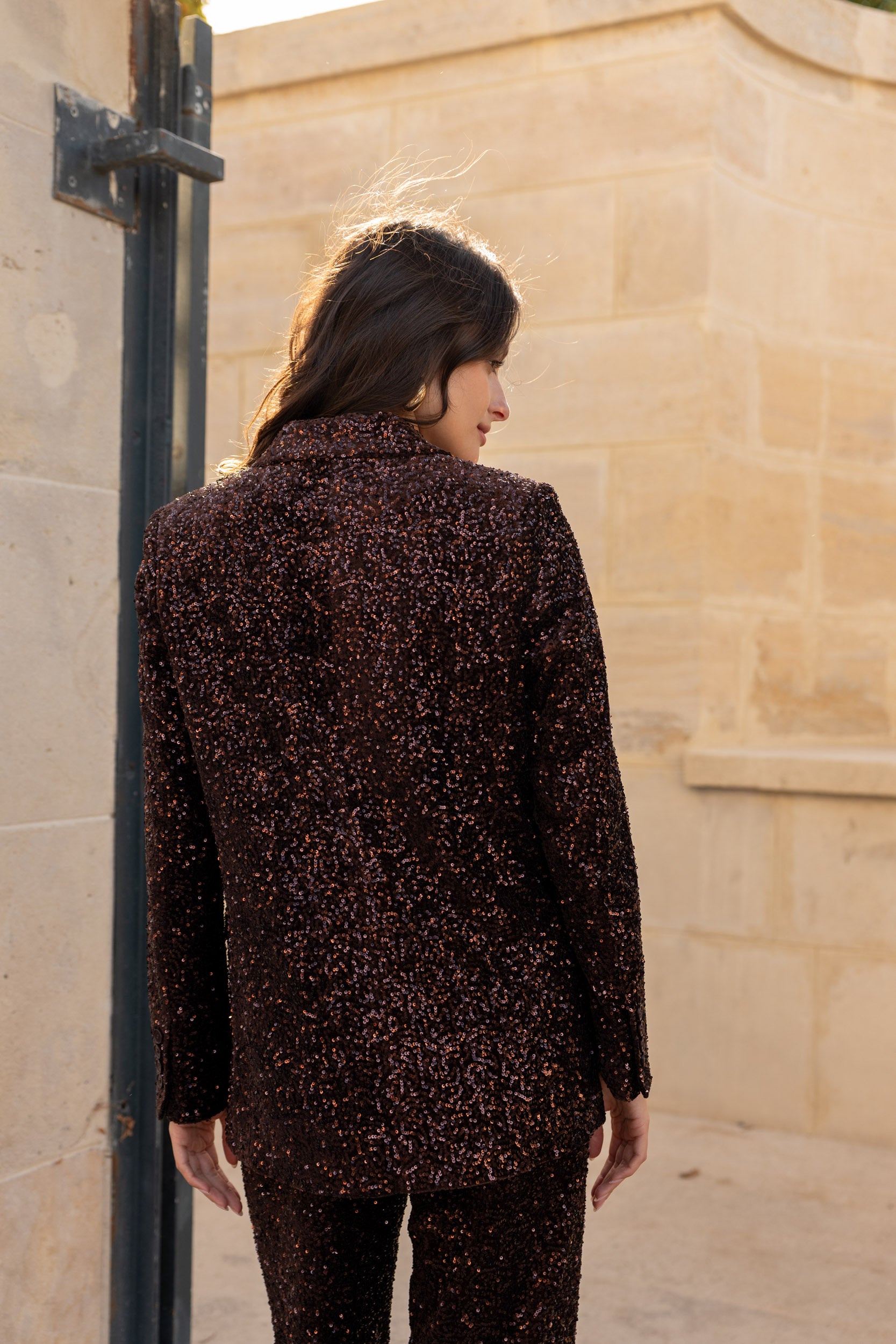 Woman wearing a patterned coat standing against a stone wall.