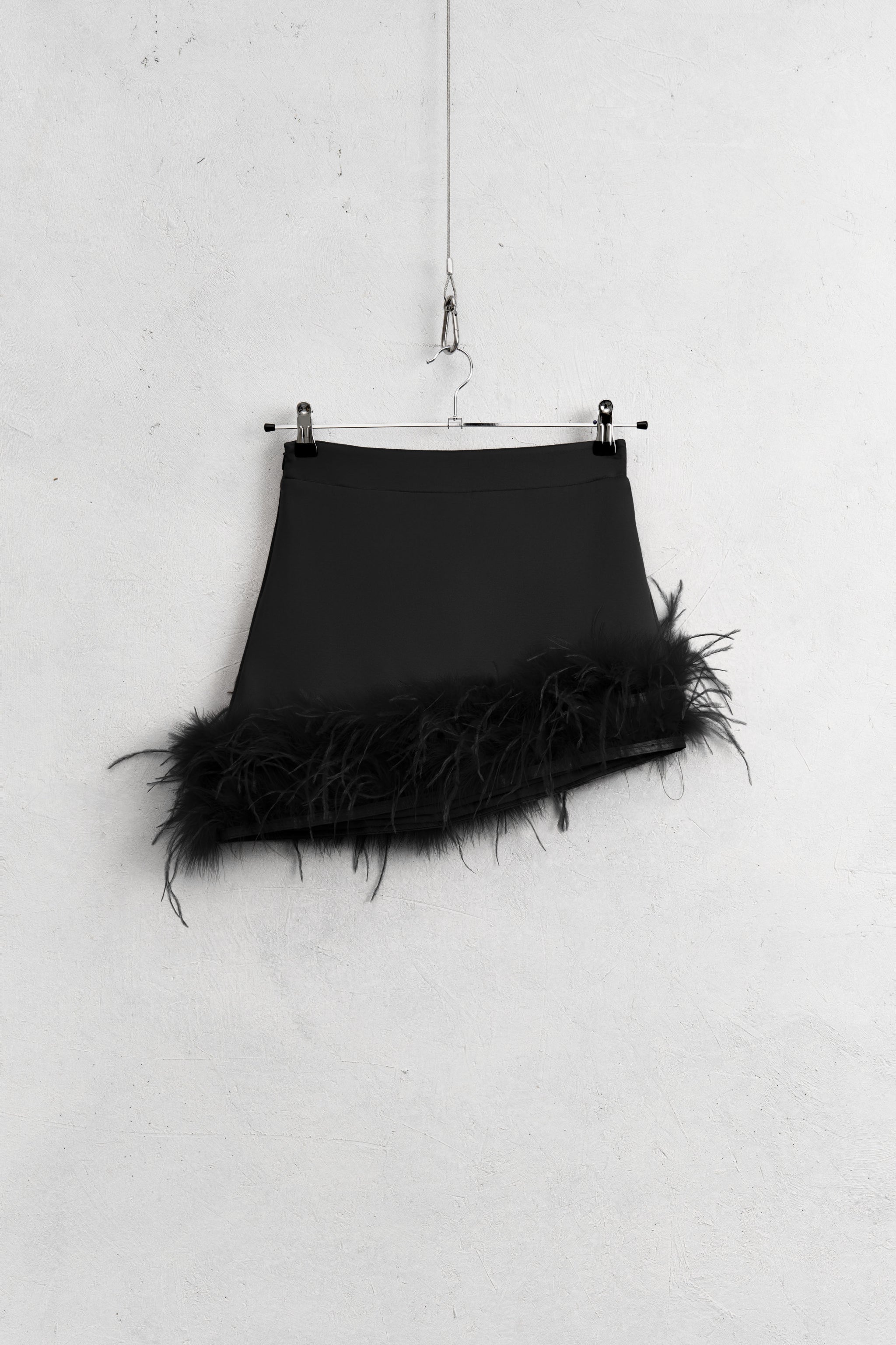 Black skirt with feathered hem on a hanger against a white wall