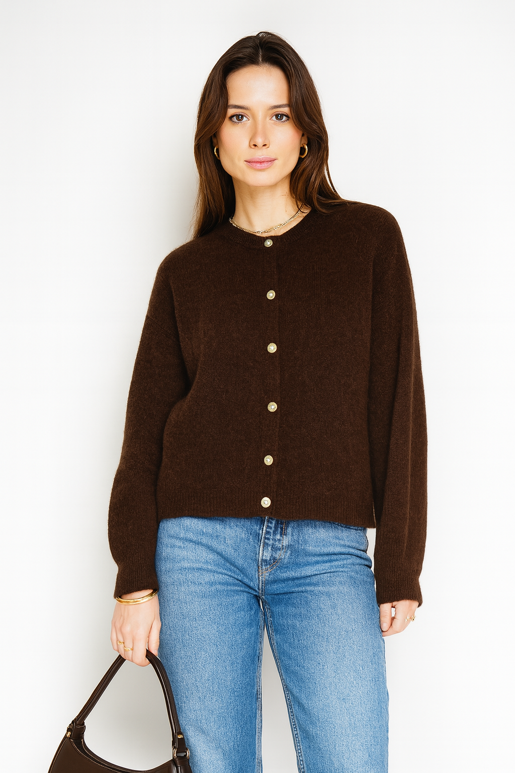 Woman wearing a brown cardigan and blue jeans against a white background