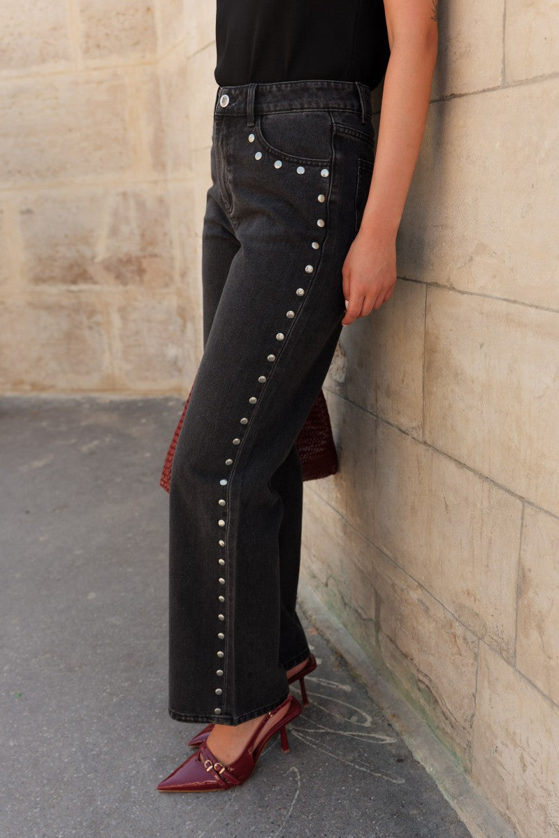 Person wearing black jeans with decorative buttons against a stone wall.