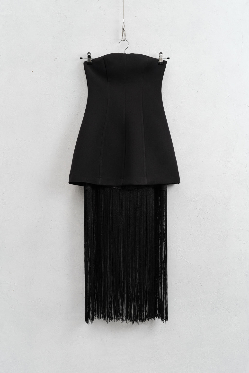 Black strapless top with fringe skirt on a hanger against a white background
