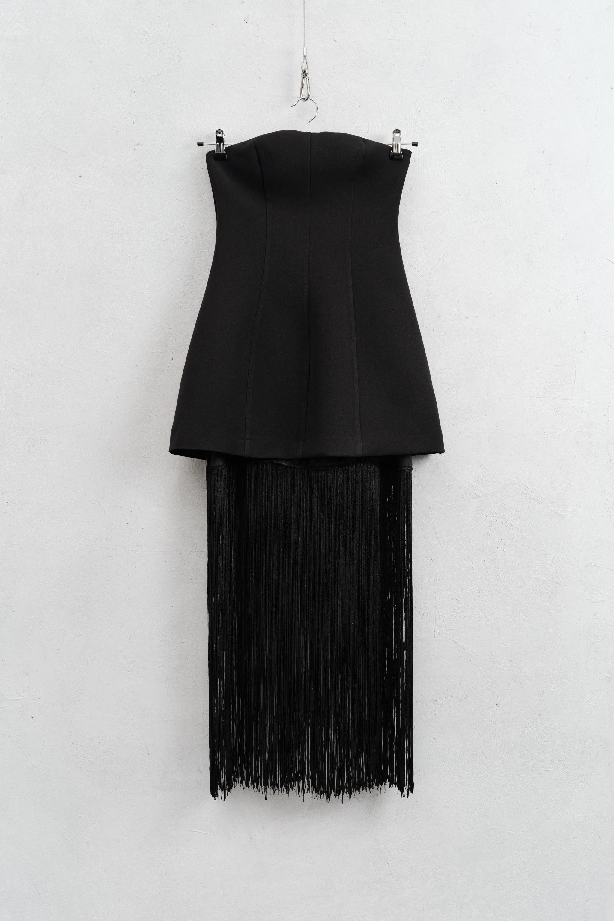 Black strapless top with fringe skirt on a hanger against a white background