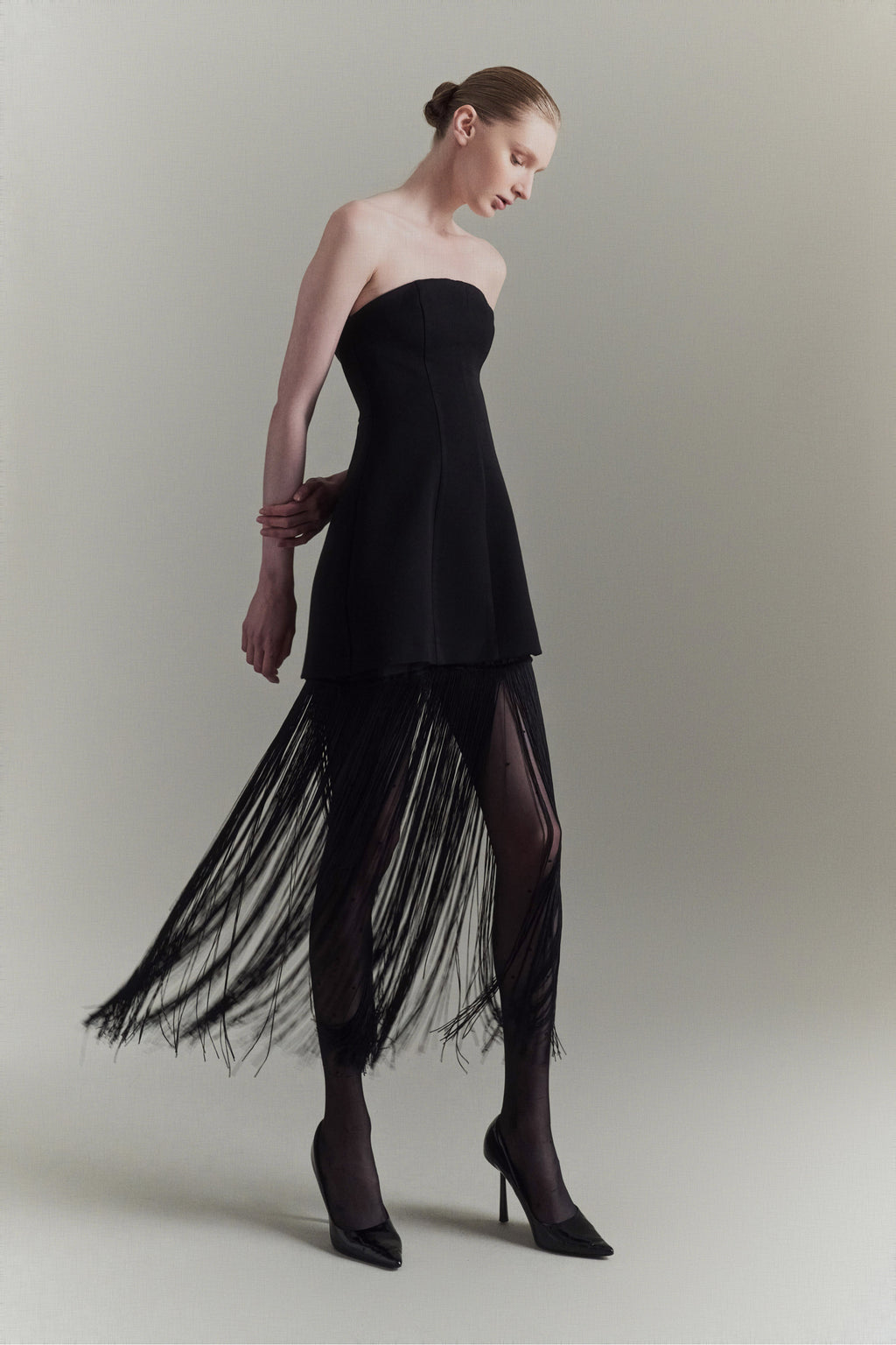 Woman wearing a black strapless dress with fringe details on a plain background