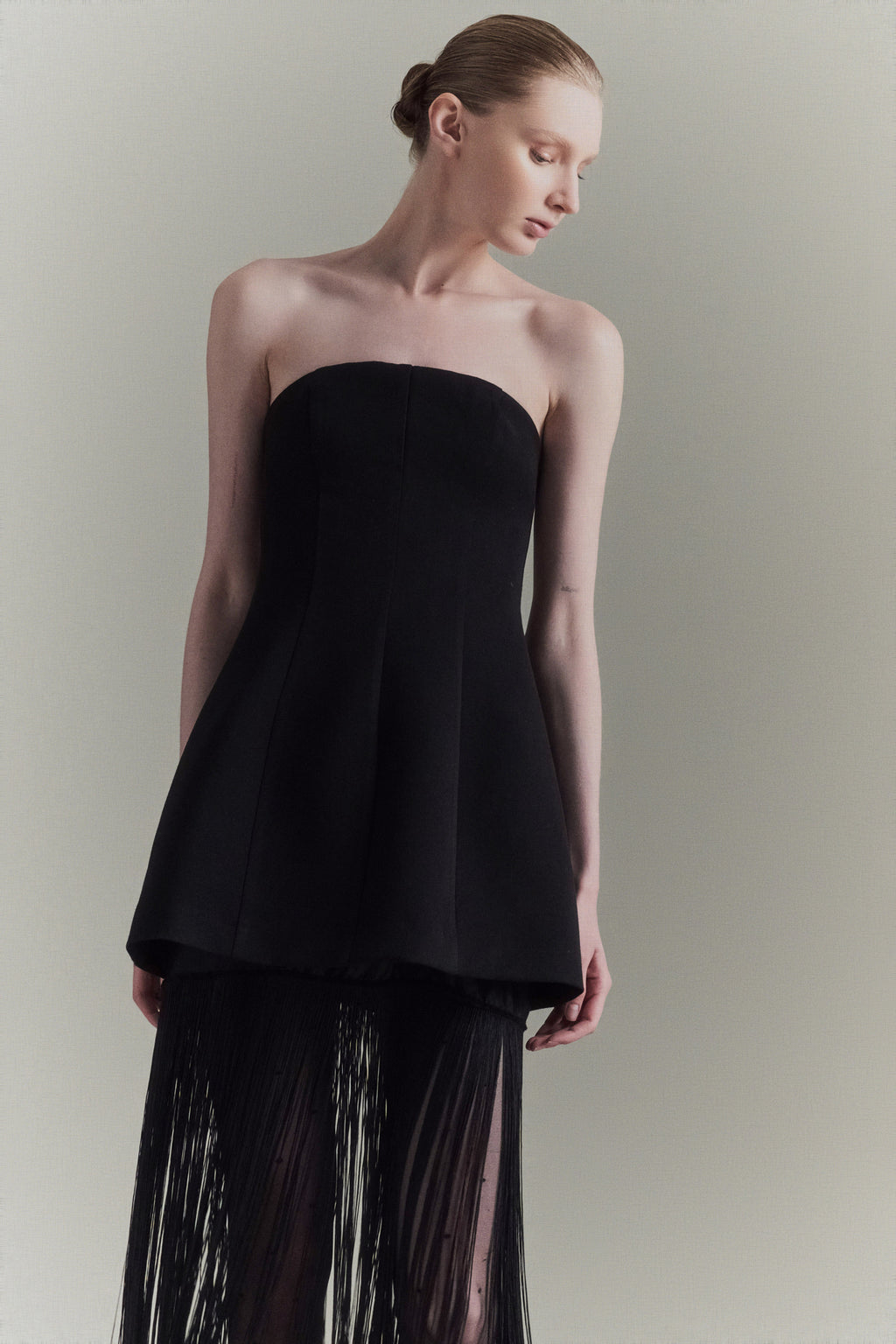 Woman wearing a black strapless top and black pants with sheer details against a plain background