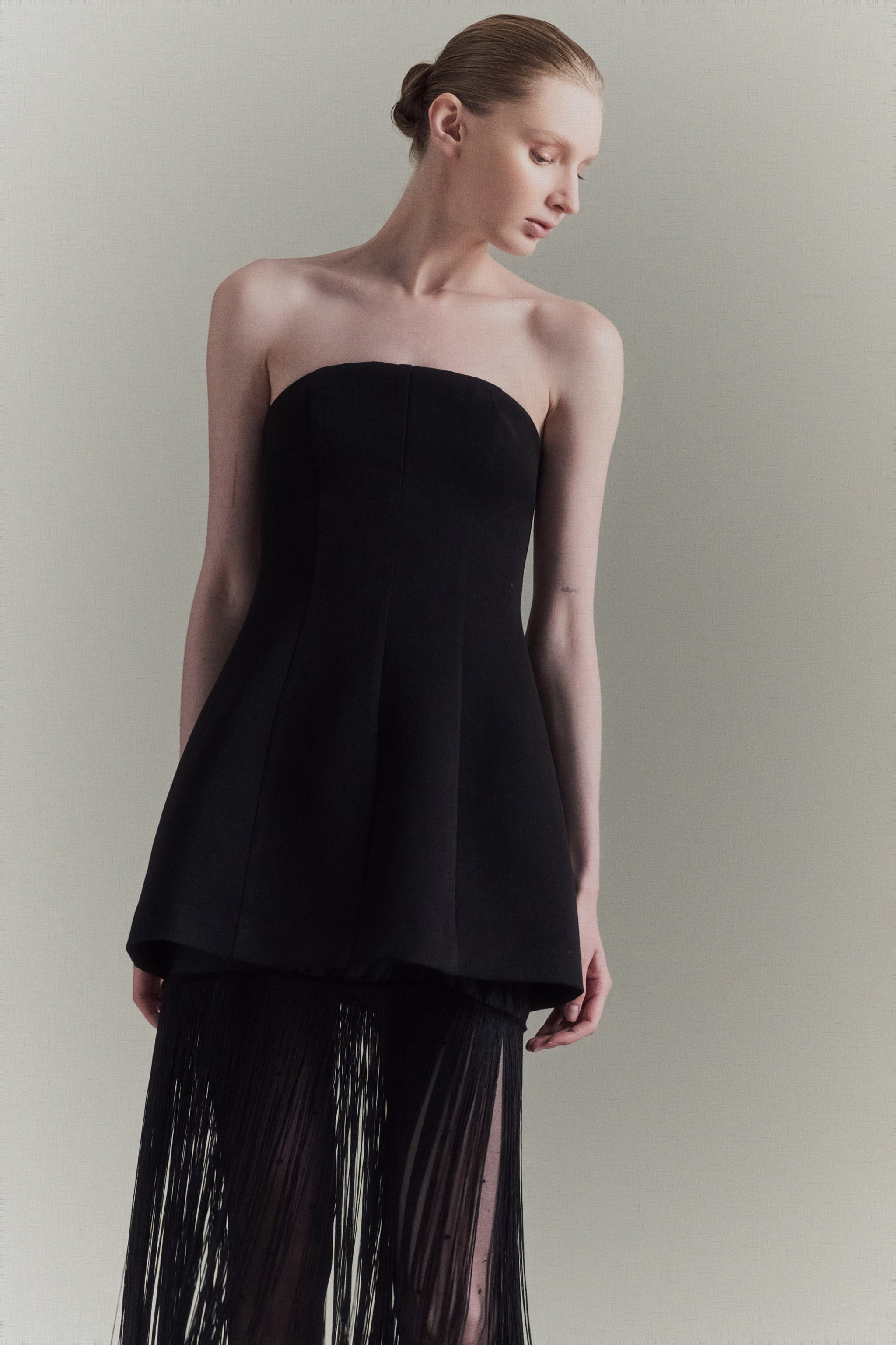 Woman wearing a black strapless top and black pants with sheer details against a plain background